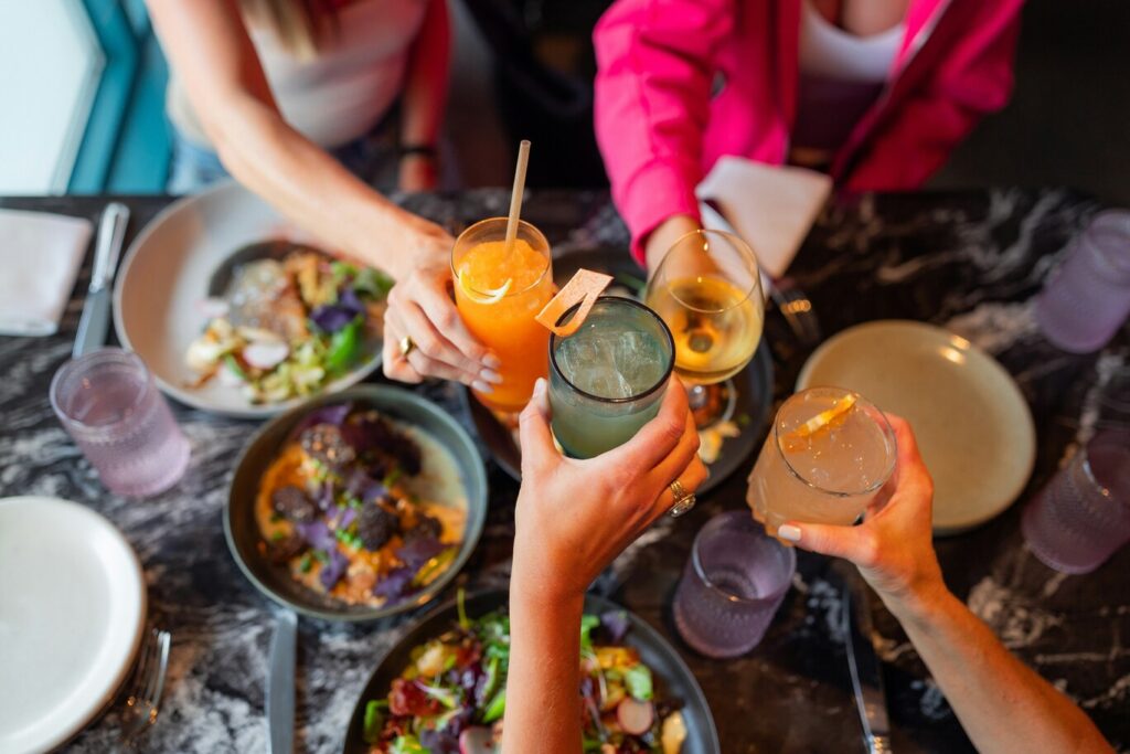 A close-up of hands raising glasses in a toast, with drinks catching the light, conveying a celebratory moment of connection, warmth, and shared enjoyment.