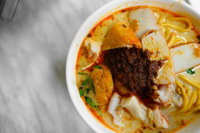 A vibrant bowl of laksa served with a generous dollop of sambal on, adding a bold splash of colour and hinting at layers of spice and depth.