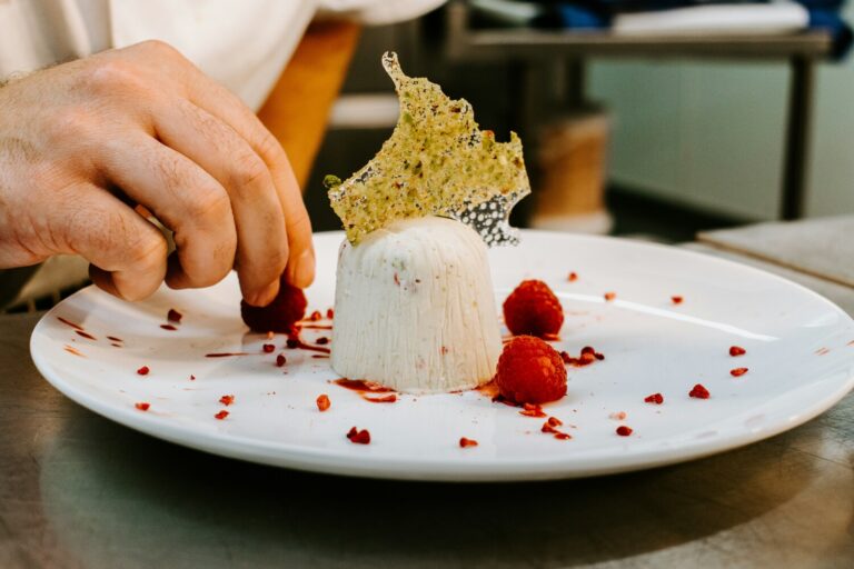 A chef’s hand carefully plating an elegant dessert, adding final details with precision to create a beautifully presented dish ready to be served.