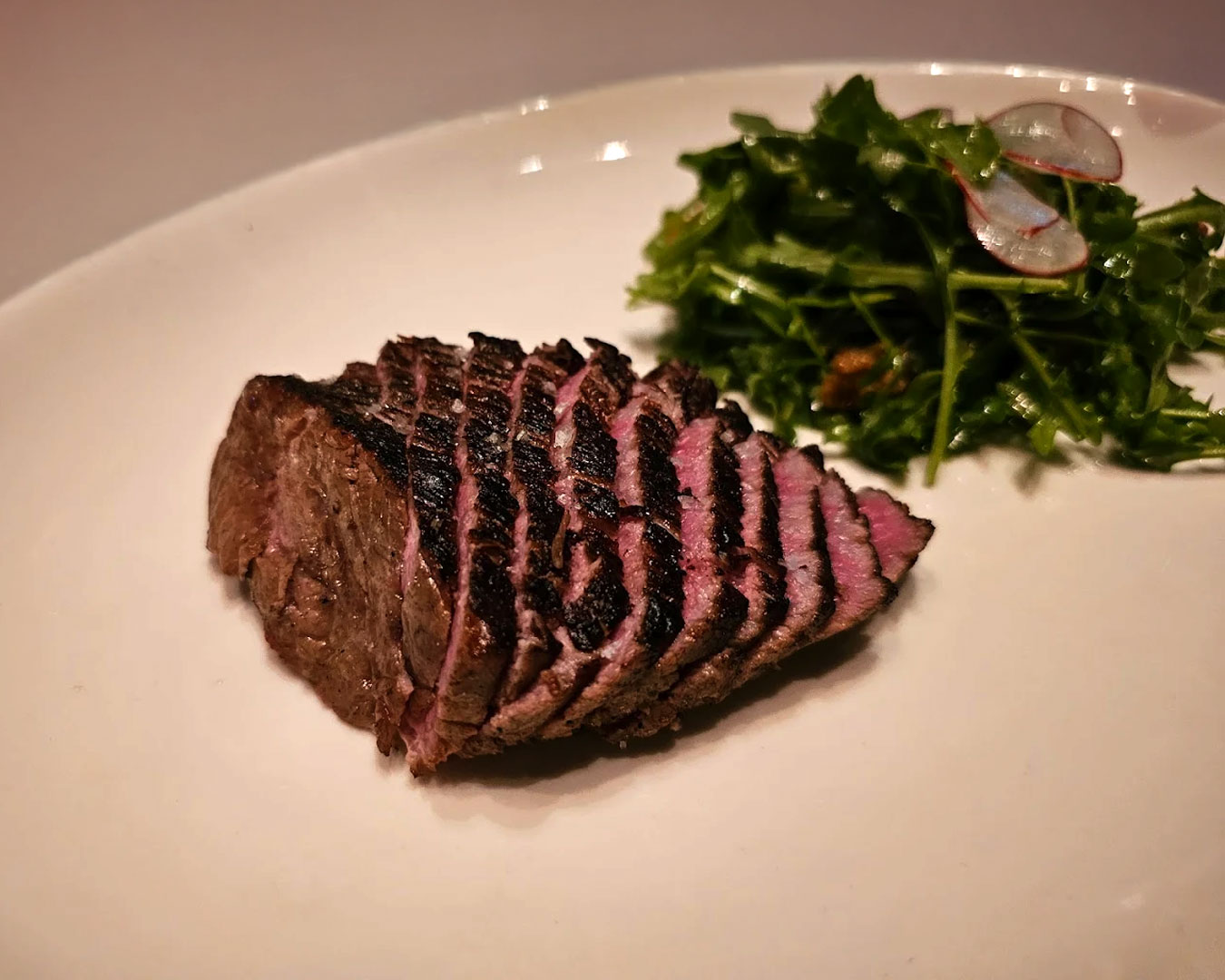 A perfectly cooked medium-rare cut of meat rests on a warm plate at Burnt Ends Restaurant, revealing a tender pink centre with a beautifully charred exterior that highlights expert grilling and rich flavour.