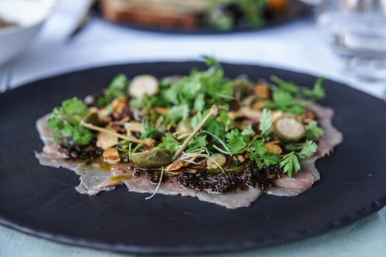Thinly sliced carpaccio draped in a light, balanced dressing, where freshness meets refinement through minimalist presentation and gentle seasoning.