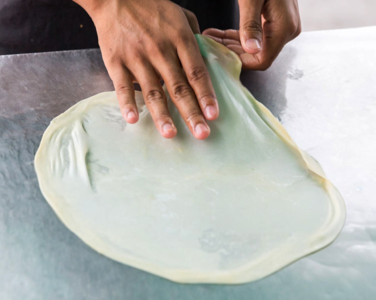 A skilled hand flips the parata dough mid-air, using centrifugal force to stretch it thin and evenly for perfect layering.