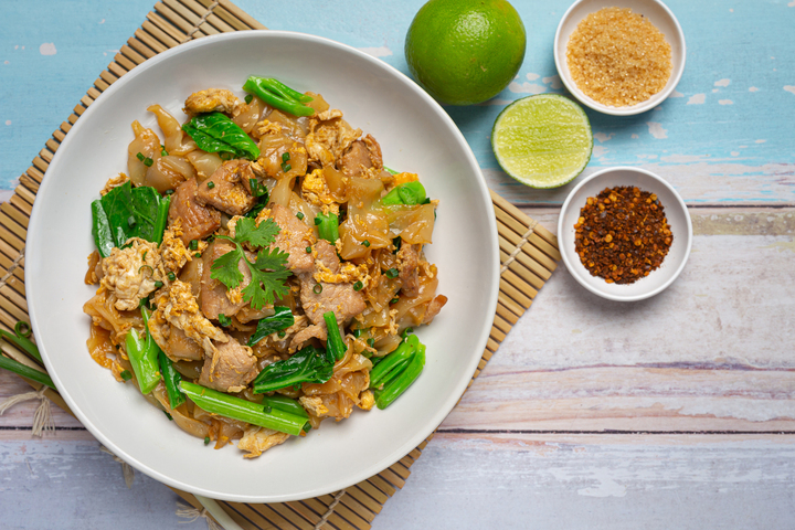 A freshly served plate of char kway teow resting on a hawker stall table, noodles lightly coated in sauce with visible prawns and chives, captured during the quiet calm after the lunch rush.