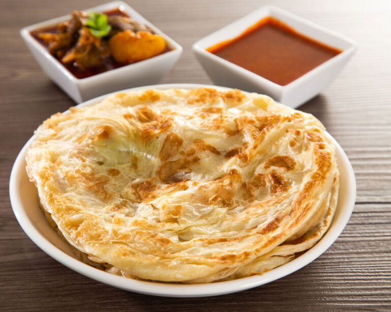 Golden, crispy roti parata served warm on a plate, paired with rich, aromatic curry, showcasing flaky layers and inviting textures.