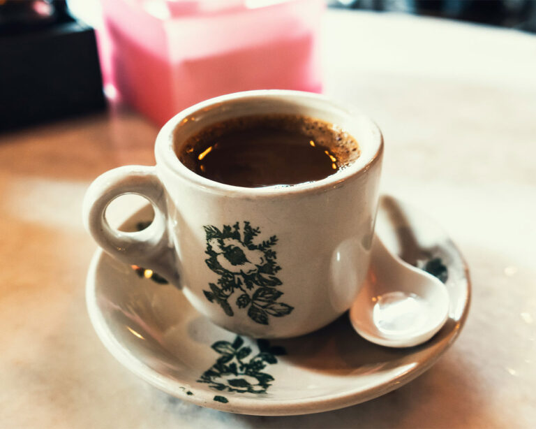 A traditional kopitiam-style coffee served in a ceramic cup, with a rich dark colour and light steam rising, placed on a simple table in a local coffee shop setting.