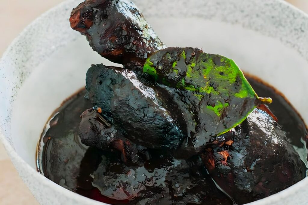 Rich, dark chicken pieces coated in thick, glossy sauce sit in a light gray bowl. A fresh green leaf garnishes the dish, highlighting its savory allure.