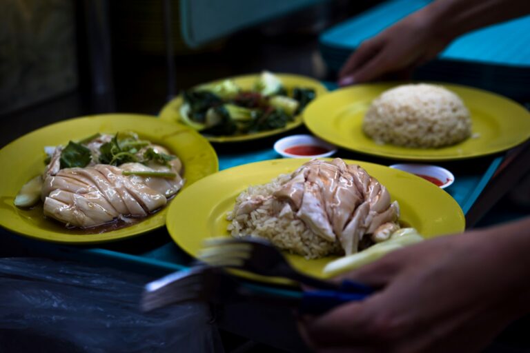 A close-up of a vendor’s hand carefully plating chicken rice, highlighting the simplicity and craftsmanship behind Singapore’s beloved hawker dish.