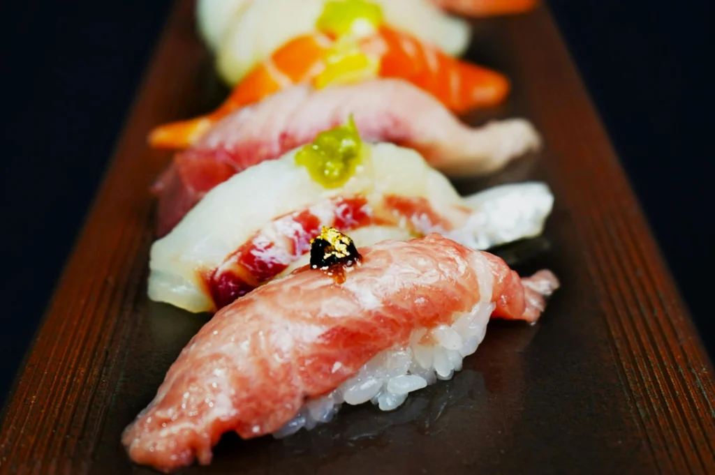 A row of elegant sushi nigiri on a wooden board, featuring vibrant fish like tuna and salmon, garnished with wasabi and gold flakes, conveying luxury.