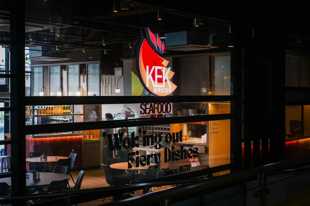 The image shows the interior of a modern seafood restaurant with a large "KEK" sign. Warm lighting and cozy seating create an inviting, relaxed atmosphere.