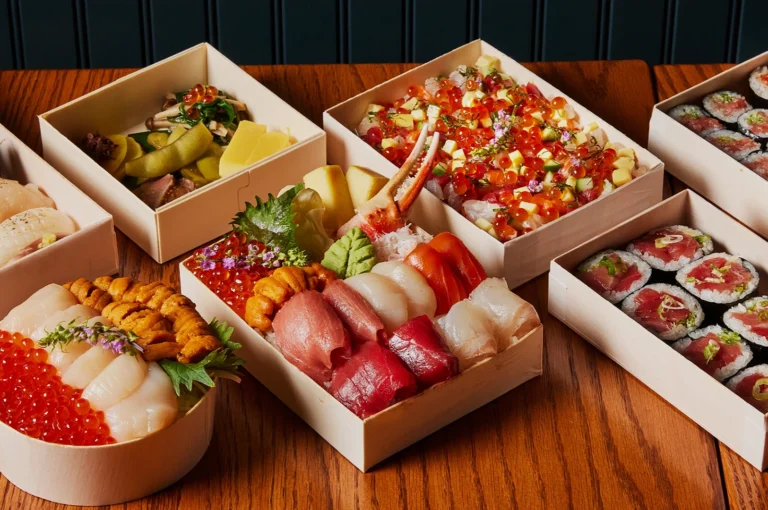 An assortment of colorful sushi boxes on a wooden table, featuring nigiri, sashimi, and rolls with vibrant fish roe, garnished with wasabi. Luxurious and inviting.