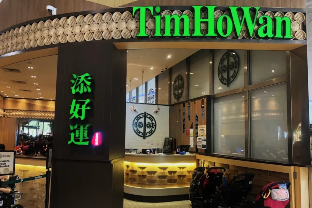 Entrance of a dim sum restaurant, Tim Ho Wan, with vibrant green signage, traditional decor, and a warm, inviting atmosphere.