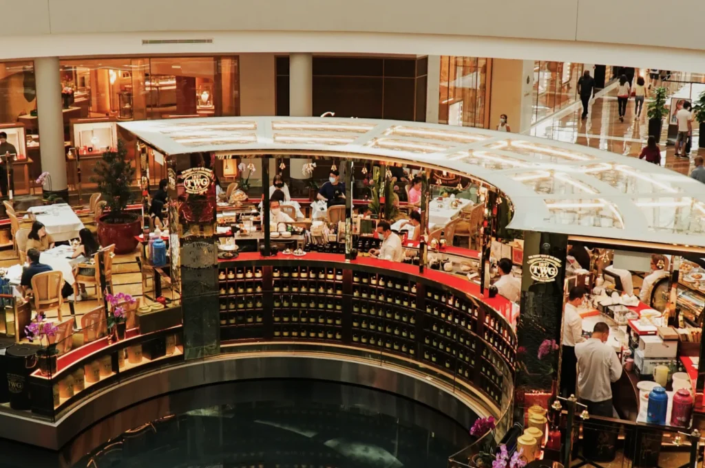 A bustling indoor café in a shopping mall, featuring a circular counter with customers seated, elegant decor, and a lively, social atmosphere.