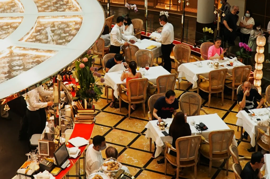 Aerial view of a bustling restaurant with wicker chairs and white tablecloths. Diners enjoy meals, while attentive waitstaff serve, creating a lively atmosphere.