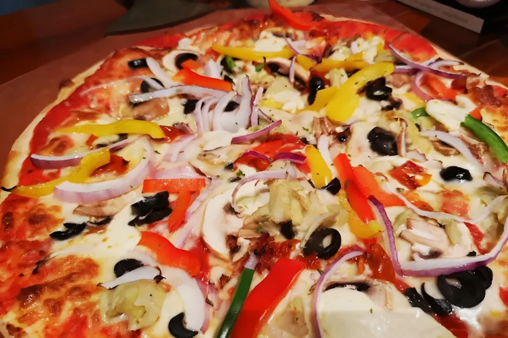 A vibrant pizza topped with colorful vegetables: red, yellow, and green bell peppers, red onion slices, mushrooms, and black olives on a cheese base