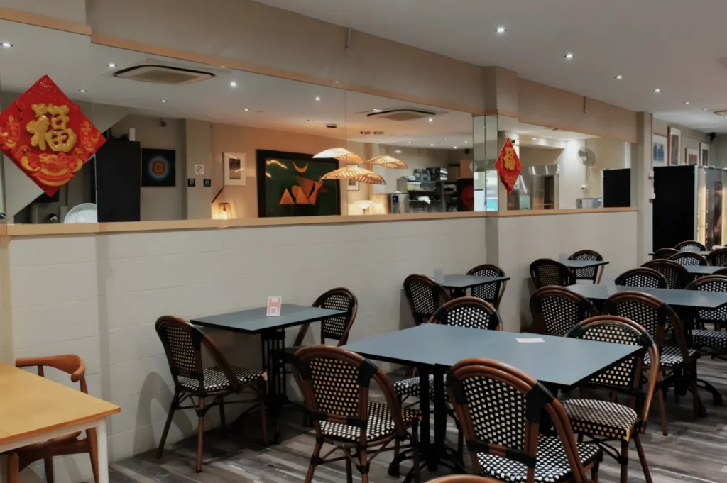 A cozy, well-lit restaurant interior with rows of tables and checkered chairs. Red Chinese decorations hang on mirrors, creating a welcoming atmosphere.