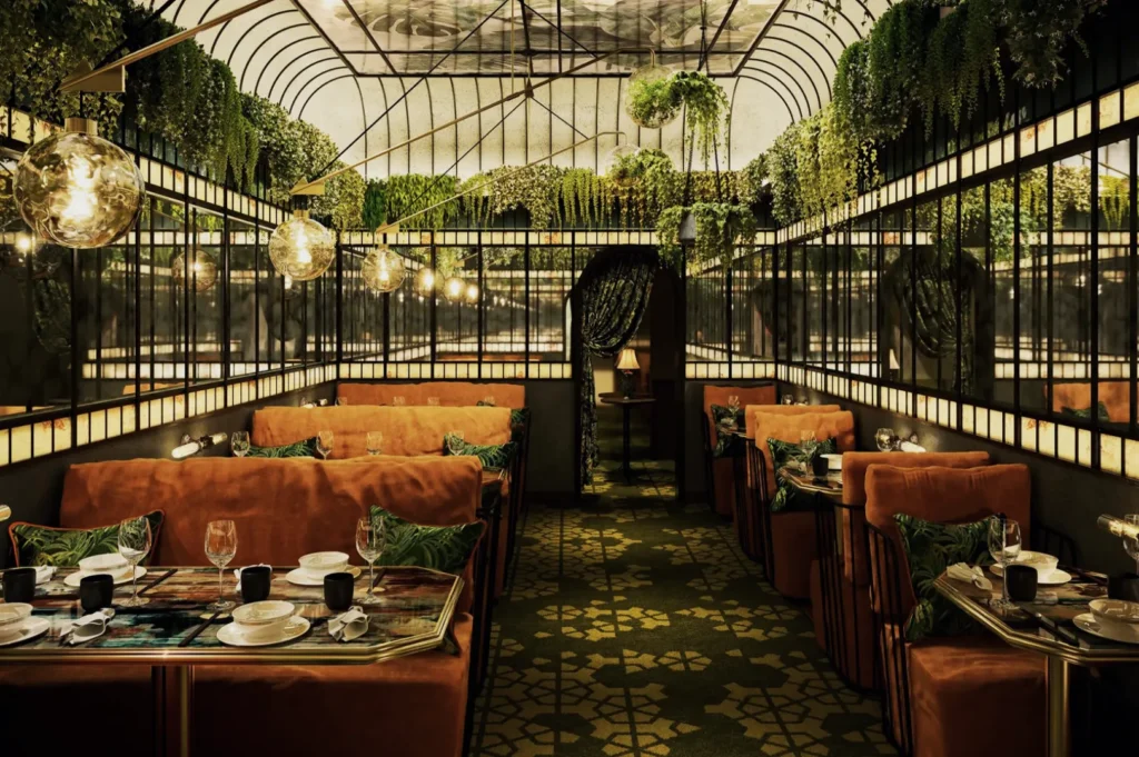 Luxurious indoor dining space with lush greenery and hanging plants, mirrored walls, warm lighting, cushioned seating, and elegant tableware.