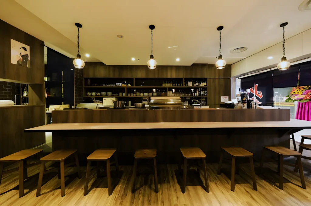 Modern, cozy cafe interior with wooden bar counter and stools, pendant lighting, shelves stocked with bottles and glasses, creating a warm ambiance.