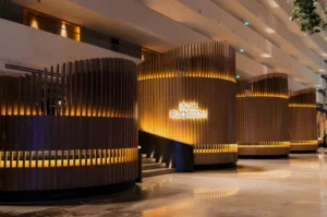 Modern lobby with warm lighting features cylindrical wooden partitions and lit signage reading "Blossom." The atmosphere is elegant and inviting.