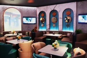 Chic lounge with plush beige and teal seating, marble accents, round mirrors, and floral arrangements. Relaxing ambiance with muted lighting and wall art.