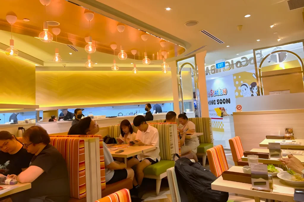 A warmly lit restaurant with striped booth seats. Patrons are engaged with menus and conversations, creating a cozy and lively atmosphere.