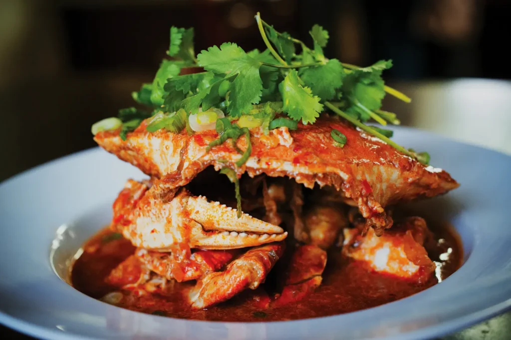 Spicy crab in a rich red sauce garnished with fresh cilantro, served on a white plate. The dish has a vibrant and appetizing appearance.