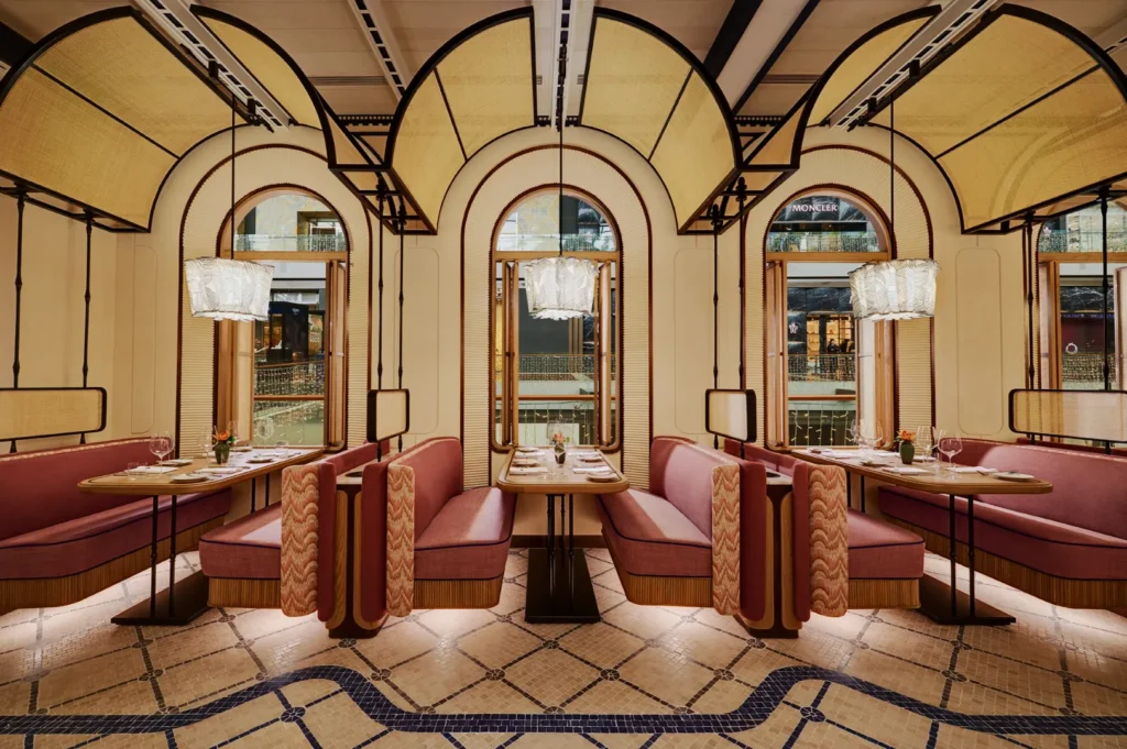 Elegant restaurant interior with art deco style. Curved ceilings, pink booth seating, arched windows, and pendant lights create a warm, sophisticated ambiance.