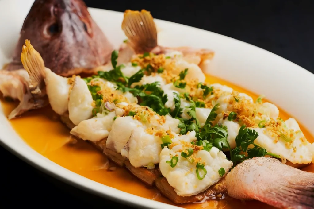 A dish featuring cooked fish with crispy skin in orange sauce, garnished with fresh herbs and green onions, served on a white plate. Luxurious and appetizing.