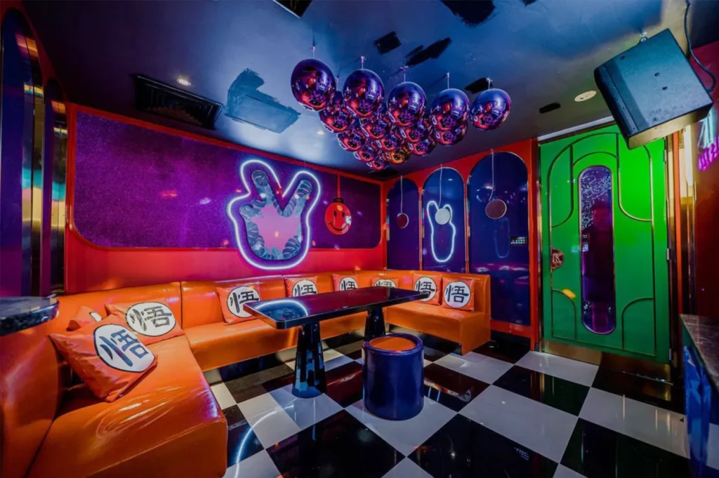Vibrant neon-lit room with orange booth seating, playful decor, and a shiny balloon ceiling. A checkered floor adds a retro, energetic vibe.
