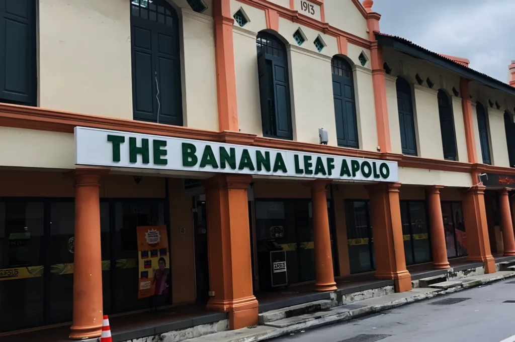 Historic building with peach columns houses "The Banana Leaf Apolo" restaurant. Green lettering on white sign, overcast sky. Inviting ambiance.