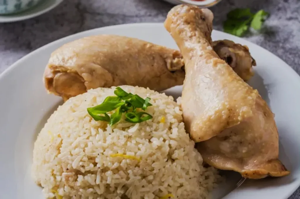 A plate of Asian-style fried rice garnished with green onions, served with two cooked chicken drumsticks, creating an inviting and savory meal.