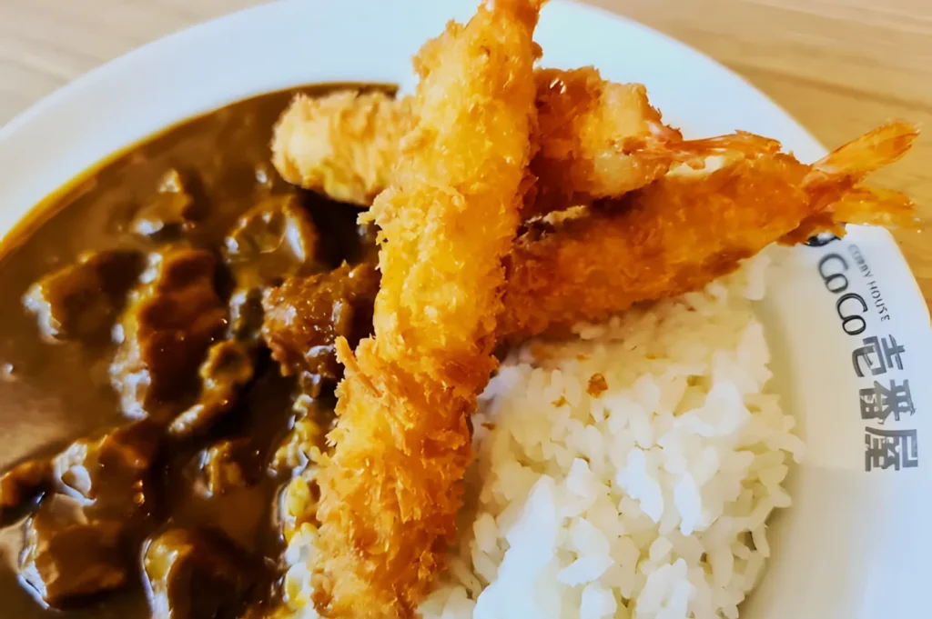 Plate of Japanese curry with rice, topped with crispy fried shrimp. The dish appears appetizing, showcasing a rich curry sauce and golden shrimp.