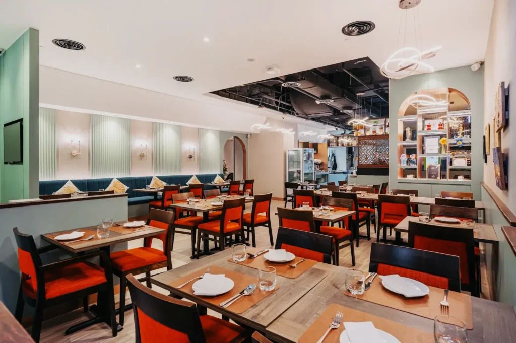 Stylish restaurant interior with neatly arranged wooden tables and red cushioned chairs. Soft lighting and modern decor create an inviting ambiance.