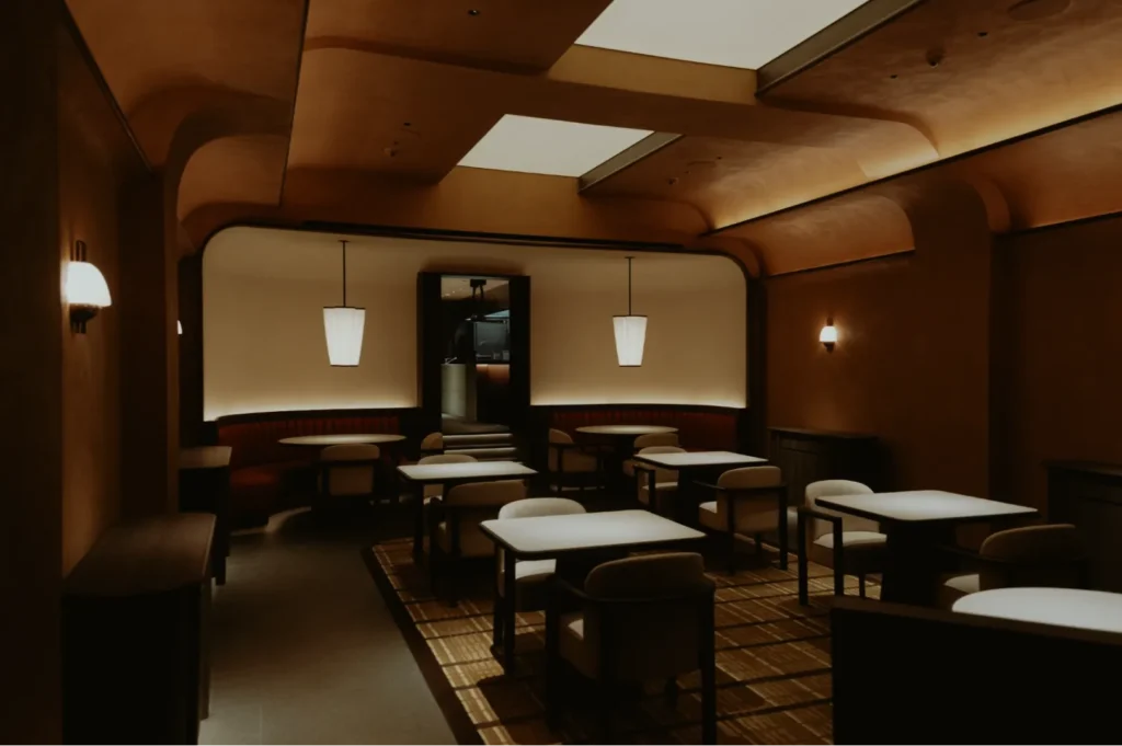 Elegant restaurant interior with warm lighting, featuring modern tables and cushioned chairs. Pendant lights and curved ceilings create a cozy ambiance.