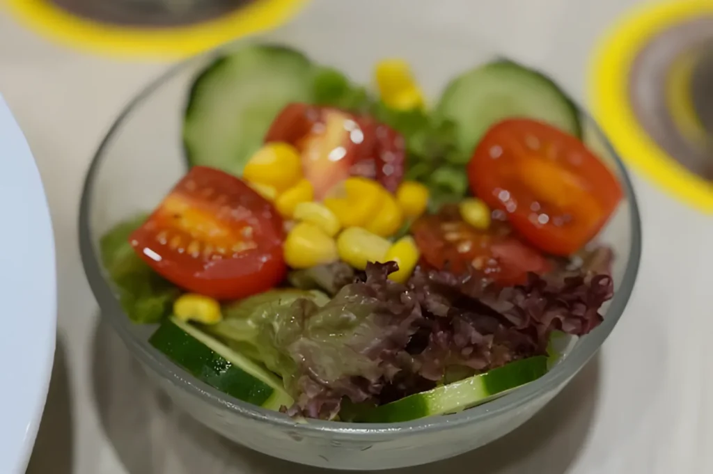 A fresh salad in a bowl featuring vibrant red cherry tomatoes, crisp green lettuce, cucumber slices, and yellow corn, creating a colorful, healthy mix.