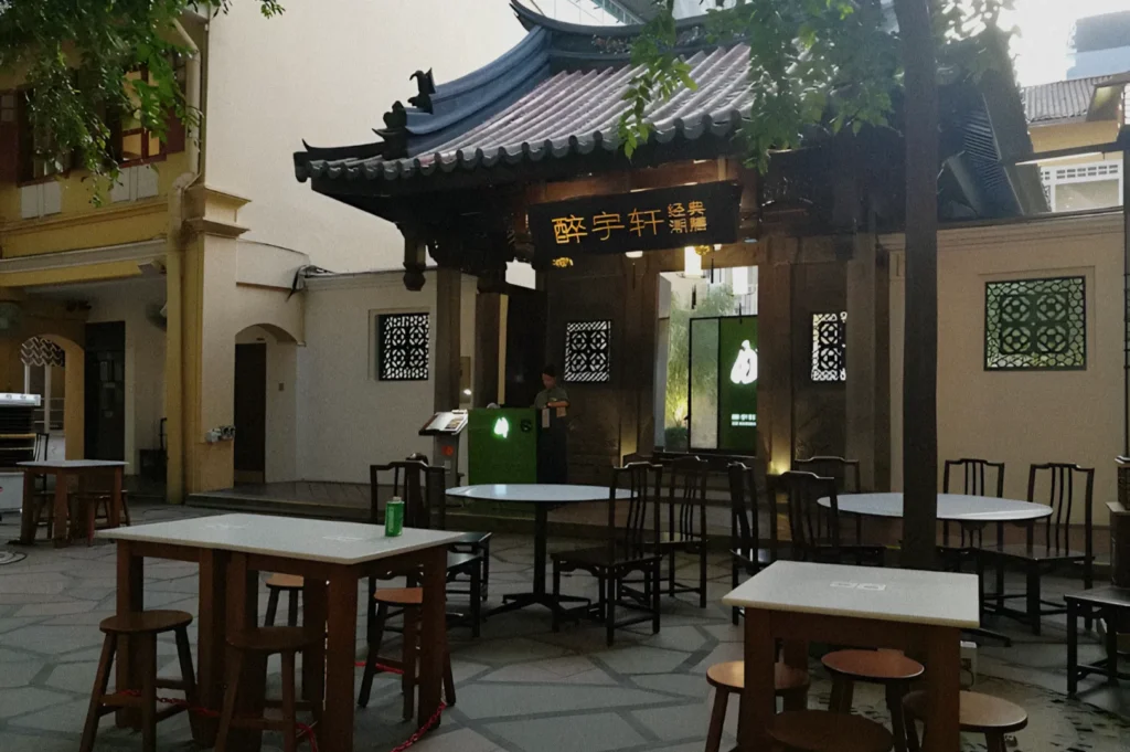 Outdoor seating area in an Asian-style courtyard with wooden tables and chairs. A pagoda-style roof and decorative wall panels add cultural charm.