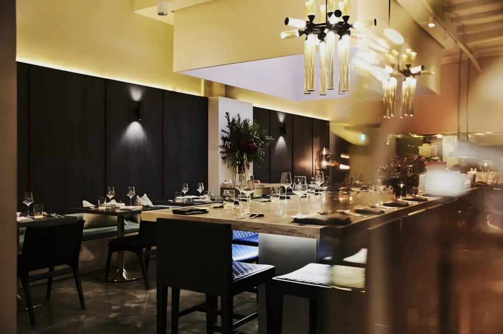 Elegant restaurant interior with a sleek modern design, featuring a large table set with glasses and napkins, soft lighting, and a warm, inviting atmosphere.