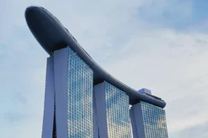 Futuristic building with three towers topped by a surfboard-like structure, under a blue sky. It exudes modernity and architectural innovation.
