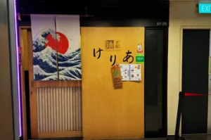 Japanese restaurant entrance featuring wooden doors with black Japanese characters. Curtains depict a wave and red sun. Menus are posted on the door.