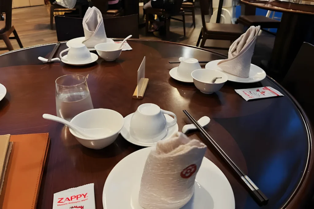 A round dining table set for a meal with neatly folded napkins, white dishes, chopsticks, and teacups on a wooden surface, creating an elegant ambiance.
