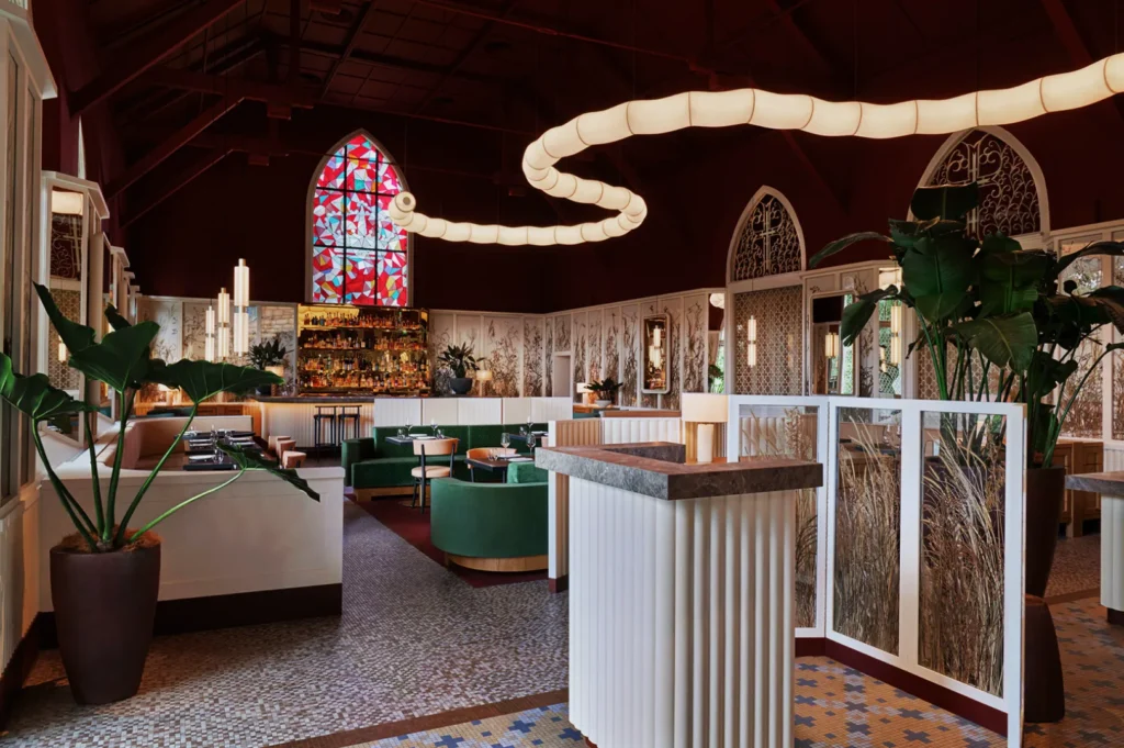 Stylish restaurant interior with deep red walls, a stained-glass window, green seating, mosaic floor, and a snake-like ceiling light, creating a cozy ambiance.
