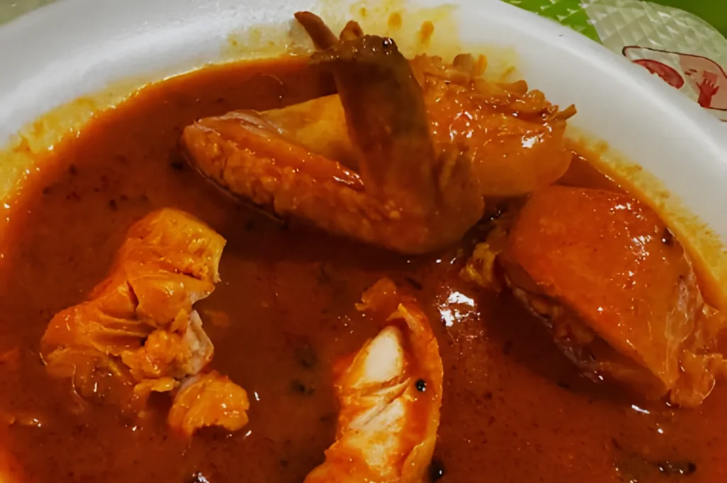A bowl of flavorful chicken curry with rich, reddish-brown sauce. Tender chicken pieces are visible, evoking a warm, comforting meal.
