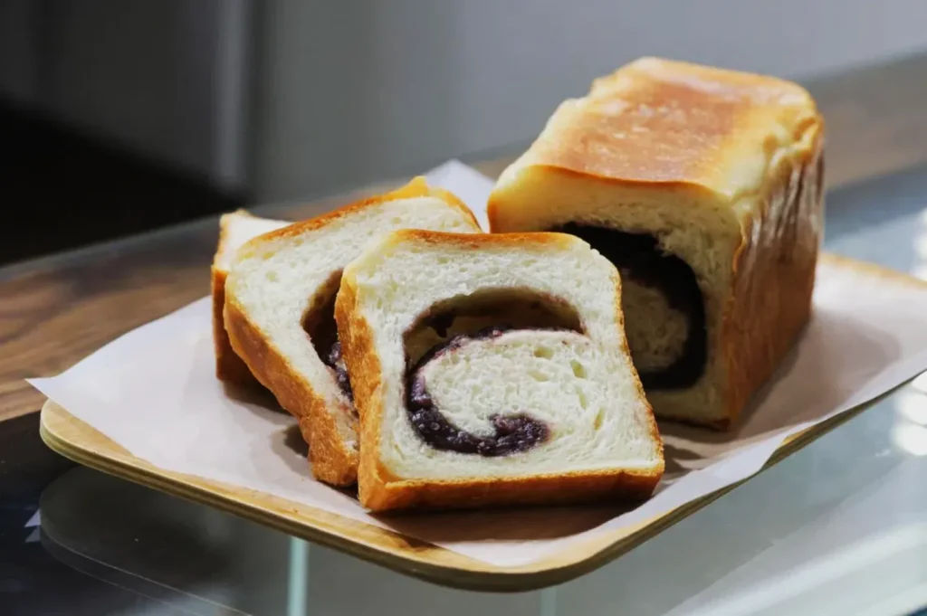 Slices of fresh bread with a visible dark swirl placed on parchment paper atop a wooden tray. The bread looks soft, inviting, and freshly baked.