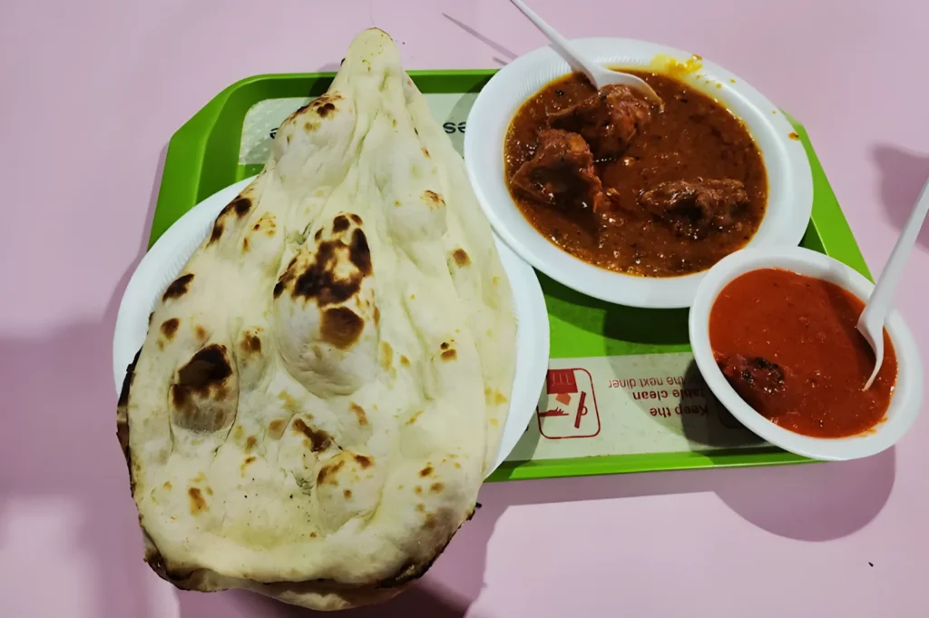 A plate of naan bread beside bowls of curry and chutney on a green tray. The scene is colorful and appetizing, suggesting a delicious Indian meal.