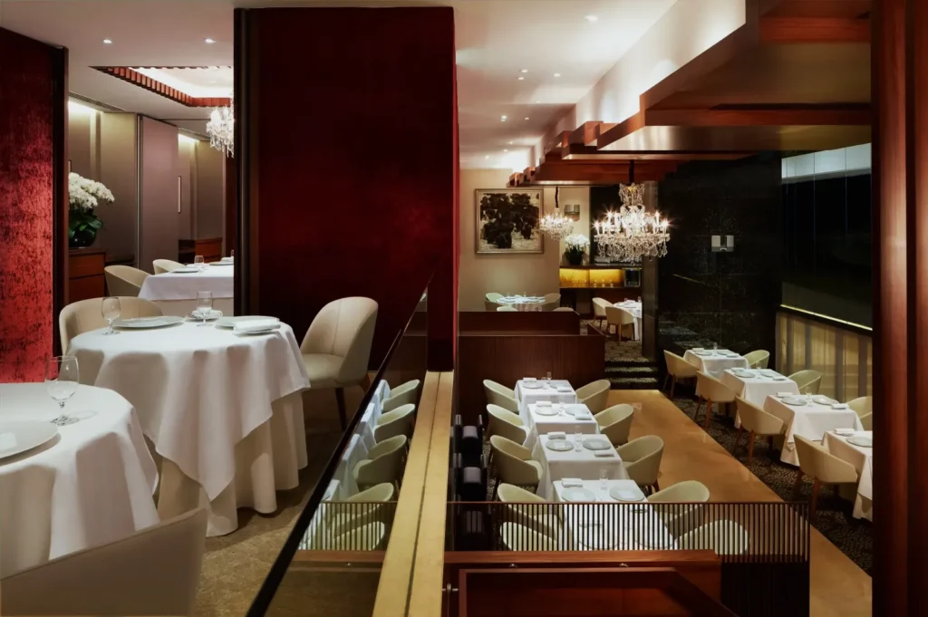 Sophisticated restaurant interior with white tablecloths and elegant chandeliers, featuring deep red walls and plush seating, creating a luxurious ambiance.