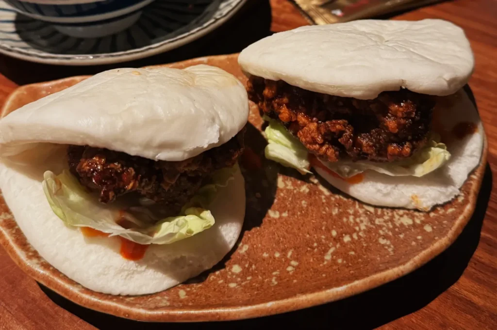Two steamed buns filled with crispy fried chicken, lettuce, and a hint of sauce sit on a rustic brown plate, exuding a warm, appetizing appeal.