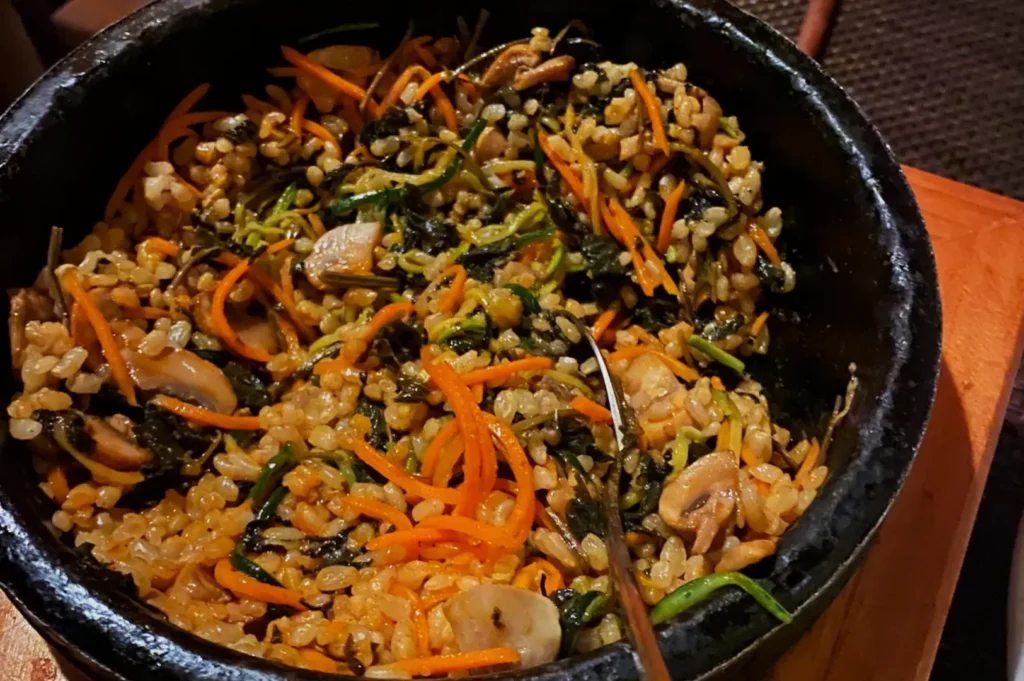 A sizzling stone bowl of bibimbap with colorful ingredients: brown rice, sliced mushrooms, vibrant shredded carrots, and greens, creating a warm, inviting meal.