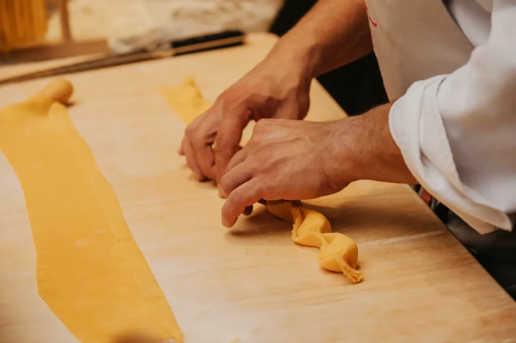 Chef's hands skillfully fold fresh pasta dough into precise shapes on a wooden surface, conveying a sense of craftsmanship and culinary focus.