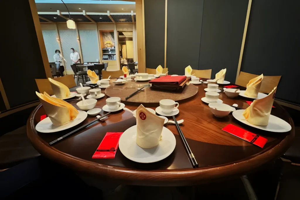 Elegant dining table set for ten with cream-colored napkins, fine china, and chopsticks. The setting is formal, warm, and inviting.