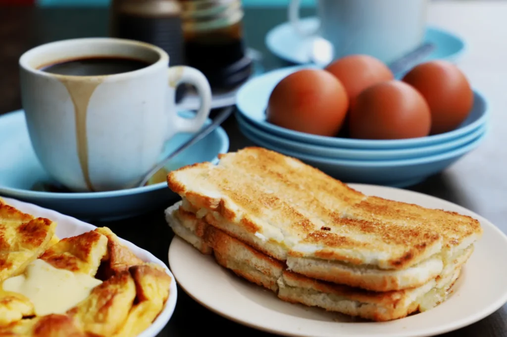 A cozy breakfast scene with a cup of coffee, toast, soft-boiled eggs on blue plates, and French toast drizzled with custard on a wooden table.