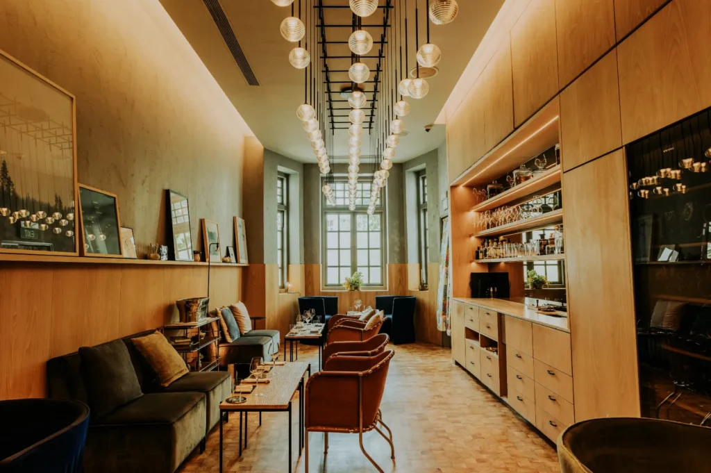 Stylish cafe interior with modern pendant lighting, cozy seating, and wooden decor. Shelves on the right hold glassware; windows allow soft daylight.